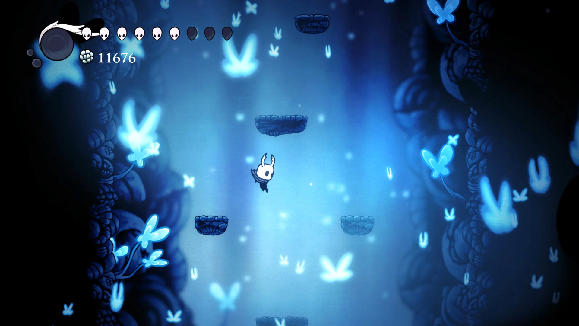 The Knight floating through a deep blue cavern filled with glowing butterflies in Hollow Knight - light and atmosphere guide the player without markers